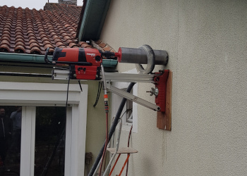 Carotteuse HILTI fixée à une façade à l'aide d'un support mobile. Autour de la couronne est disposé le système limitant la poussière lors du carottage.