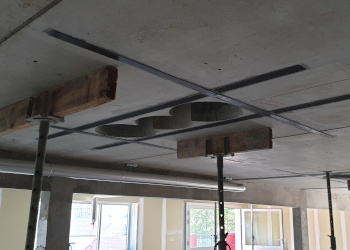Des bandes de carbones sont fixées à un plafond en béton afin de le renforcer. Les bandes de carbone sont disposées afin de former un grand rectangle dans lequel on voit trois carottages. Deux étais sont disposés de part et d'autre de l'ouvrage afin de soutenir le plafond durant l'opération.