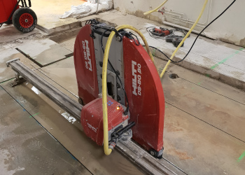 Scie murale HILTI, fixée sur son rail, utilisée pour découper une dalle au sol.