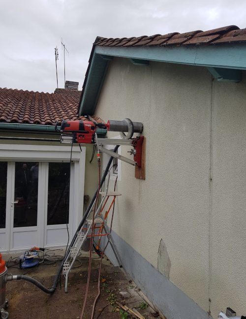 Carotteuse HILTI fixée à une façade à l'aide d'un support mobile. Autour de la couronne est disposé le système limitant la poussière lors du carottage.